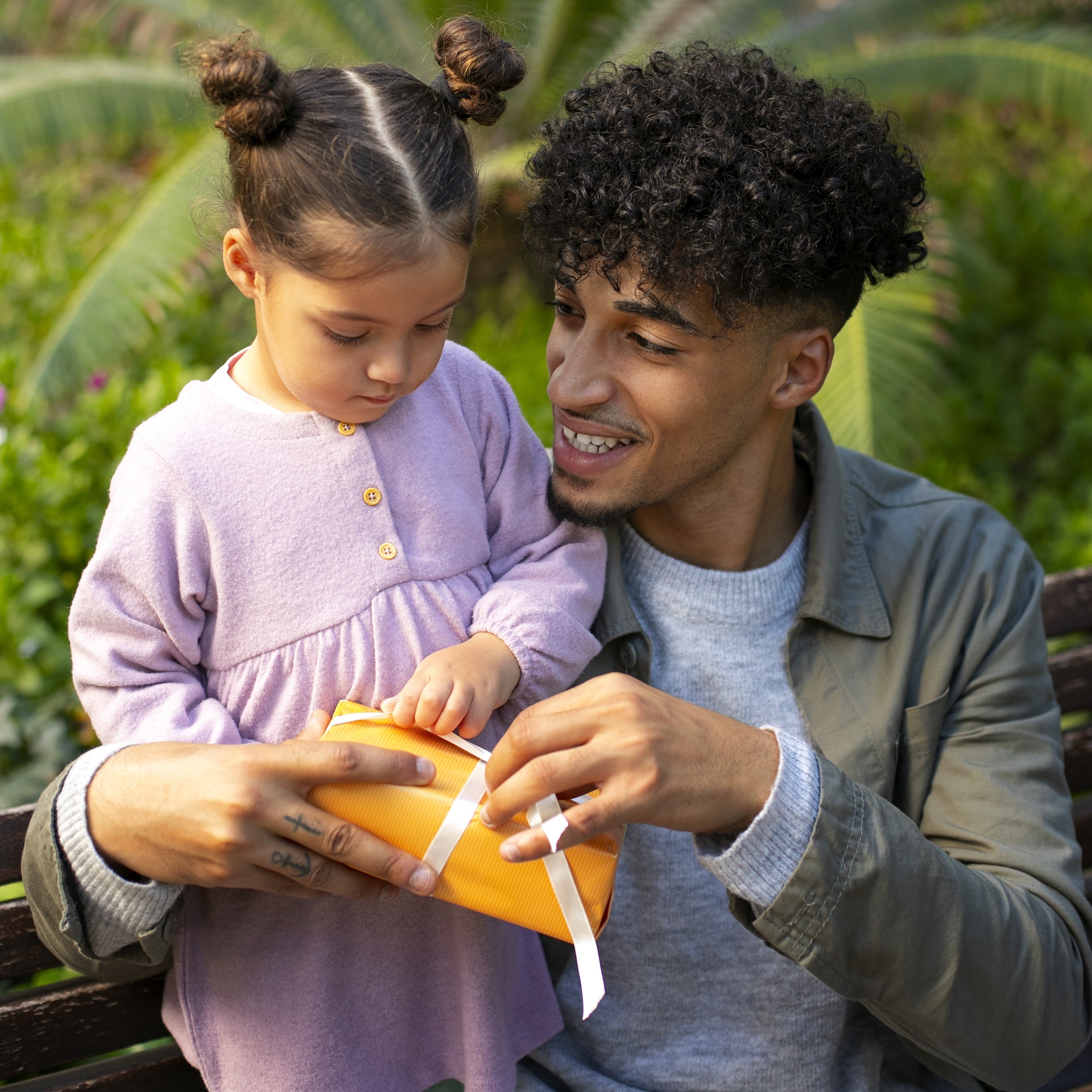 A Black man helps his daughter unwrap a gift