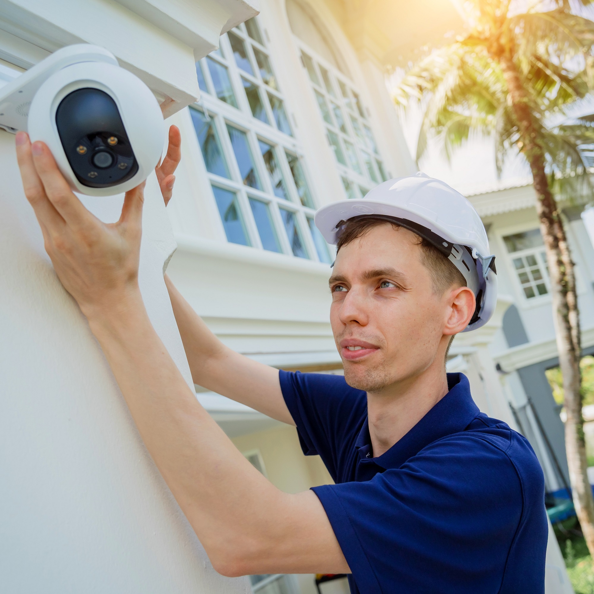 A technician installs a CCTV camera on the facade of a residential building.