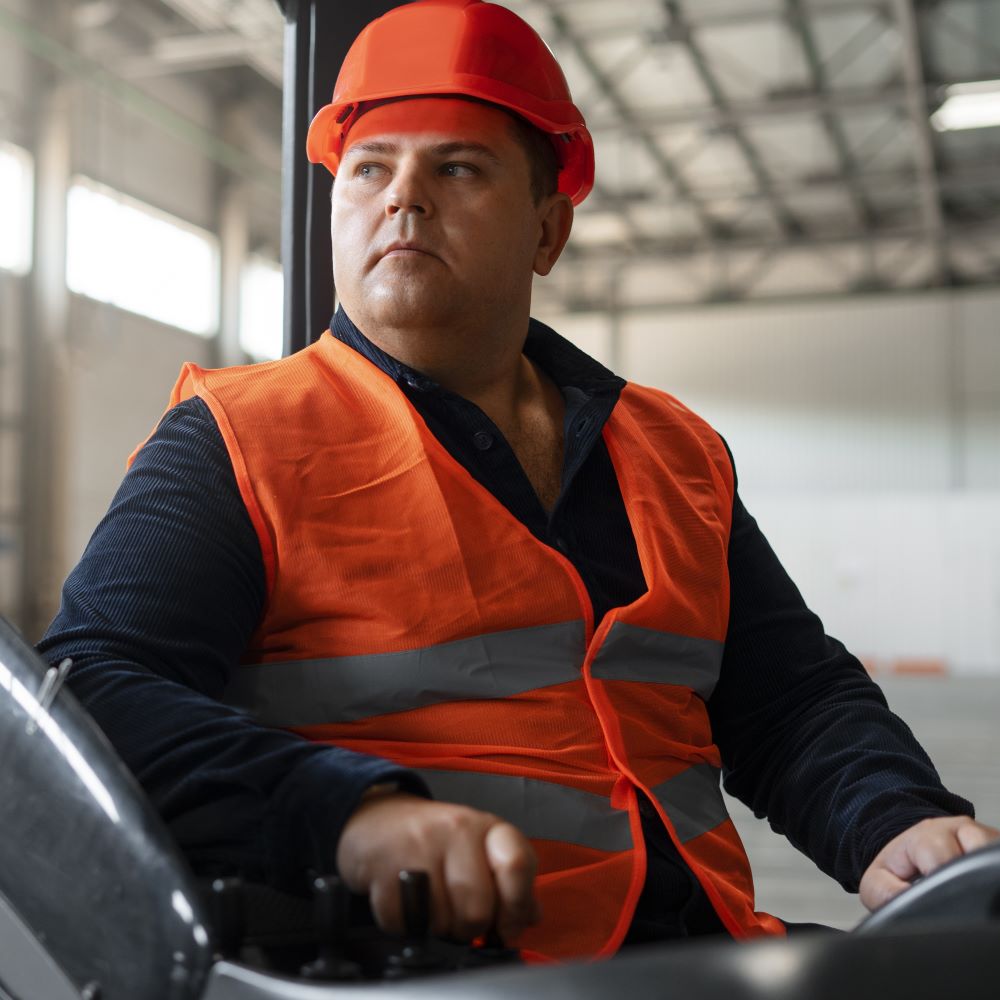 A large man in an orange high vis vest operates heavy machinery at his distribution business
