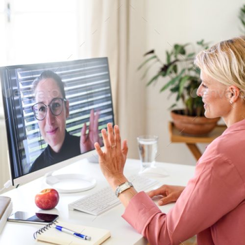 Young businesswoman having video call on computer in home office, waving.